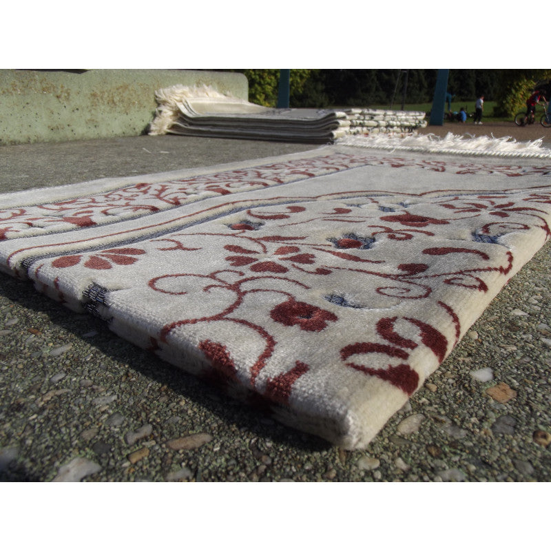 Tapis de prière Sana Edition avec motif jardin, fond blanc et couleur terracotta, visible avec détails de design floral.